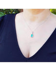 Woman wearing a 1.70 ct. Muzo Colombian emerald pendant with a diamond halo in 18K white gold.