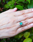 Hand wearing a ring with a green gemstone against a leafy background