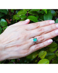 Hand wearing a ring with a green gemstone against a leafy background