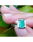 A natural emerald ring on a hand with a green leafy background