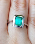A solitaire Muzo colombian emerald solitaire ring in 18k white gold on a person's finger.