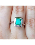 A solitaire Muzo colombian emerald solitaire ring in 18k white gold on a person's finger.