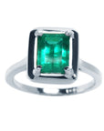 This Muzo colombian emerald solitaire ring displays its topside view of the rectangular emrald-cut prong set in 18k white gold.