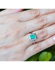 Hand wearing a white gold ring with a natural emerald gemstone against a natural background