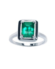 This Muzo Colombian emerald solitaire ring features a rectangular emerald-cut stone set in prongs of 18k white gold.