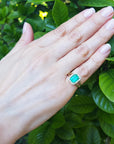 Hand wearing a May's birthstone ring for women against a leafy background.