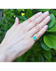 Emerald-cut Muzo Colombian emerald ring with diamond halo and split shank in 14k yellow gold on a hand.