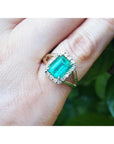 An emerald-cut natural colombian emerald ring for women with a halo diamond made of 14k yellow gold.