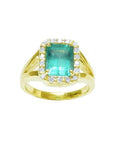 This emerald-cut Muzo Colombian emerald ring for women has a halo of natural diamonds and is crafted in 14k yellow gold.