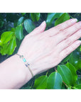 A woman's and wearing a natural Muzo colombian emerald bracelet with green leaves in the background.