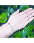 Woman's hand wearing a 14K yellow gold bracelet with a rectangular Colombian emerald and diamond halo.