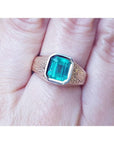 A 14k yellow gold men's ring with a natural Muzo colombian emerald bezel set worn on a finger.
