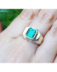 A 14k yellow gold ring for men with a bezel set square natural colombian emerald worn on a hand.