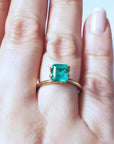 Emerald-cut Muzo Colombian emerald ring with a medium deep bluish-green stone on a gold band.