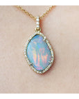 Opal pendant necklace on a gold chain against a beige skin background.