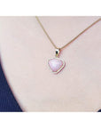 Pink heart-shaped opal pendant on a gold chain worn by a person.