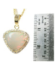 Triangular Australian white opal pendant with red fire, diamond halo, and 14K yellow gold chain, next to a ruler.