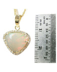 Triangular Australian white opal pendant with red fire, diamond halo, and 14K yellow gold chain, next to a ruler.