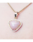 Heart-shaped pink gemstone pendant on a gold chain against a light pink skin background.