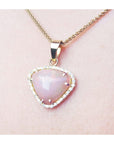 Heart-shaped pink gemstone pendant on a gold chain against a light pink skin background.