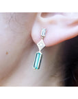 A person wearing a baguette cut colombian emerald and diamond earring.