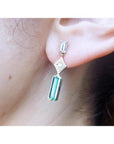 A person wearing a baguette cut colombian emerald and diamond earring.