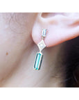 Close-up of a person wearing a baguette cut emerald earring.