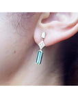 1.05 carat natural baguette cut emerald drop earrings in 14K gold, worn on an ear.