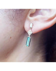 1.05 carat natural baguette cut emerald drop earrings in 14K gold, worn on an ear.