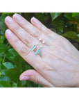 1.05 carat natural baguette cut emerald earrings in 14K gold, held against green foliage.