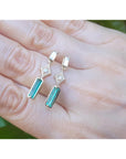 Emerald earrings with diamond stones on a hand against a blurred green background