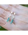 14K gold baguette emerald drop earrings with diamond accents on a hand.