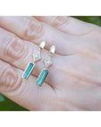 14K gold baguette emerald drop earrings with diamond accents on a hand.