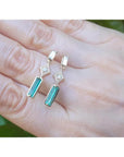 14K gold baguette emerald drop earrings with diamond accents on a hand.