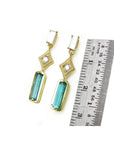 14k yellow gold earrings with Colombian emeralds and diamonds next to a ruler for size reference on a white background