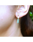 14K gold baguette cut emerald drop earrings with diamond accents on a woman's ear.
