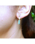 14K gold baguette cut emerald drop earrings with diamond accents on a woman's ear.