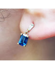 14K yellow gold earrings with emerald cut blue sapphires dangling from baguette diamonds.