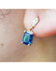 Gold earring with a blue natural sapphire and tapered baguette diamond worn on an ear