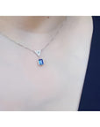14K white gold necklace with a dangling emerald-cut blue sapphire and pave diamond trillion pendant.