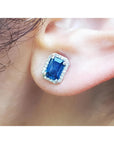 Natural blue sapphire stud earrings emerald cut halo diamond 14k white gold, on a person's ear