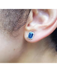 Emerald cut natural blue sapphire stud earring with diamond halo in 14K white gold on an ear.