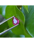 1.24 carat natural Burmese ruby, pear cut, medium red, held by tweezers on a green leaf.