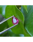 1.24 carat natural Burmese ruby, pear cut, medium red, held by tweezers on a green leaf.