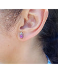 A woman wearing a cabochon pink sapphire earring with a blurred background.