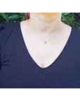 Woman wearing a vibrant pear-shaped emerald necklace with diamond halo on a 14K yellow gold chain.