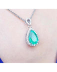 Teardrop-shaped emerald necklace on a person's neck with a blue background.