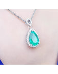 Pear-cut Colombian emerald pendant with diamond halo on 18K white gold chain, worn on a blue top.
