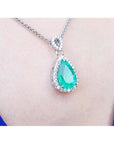 Pear-cut Colombian emerald pendant with diamond halo on 18K white gold chain, worn on a blue top.