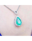 Pear-cut Colombian emerald pendant with diamond halo on 18K white gold chain, worn on a blue top.